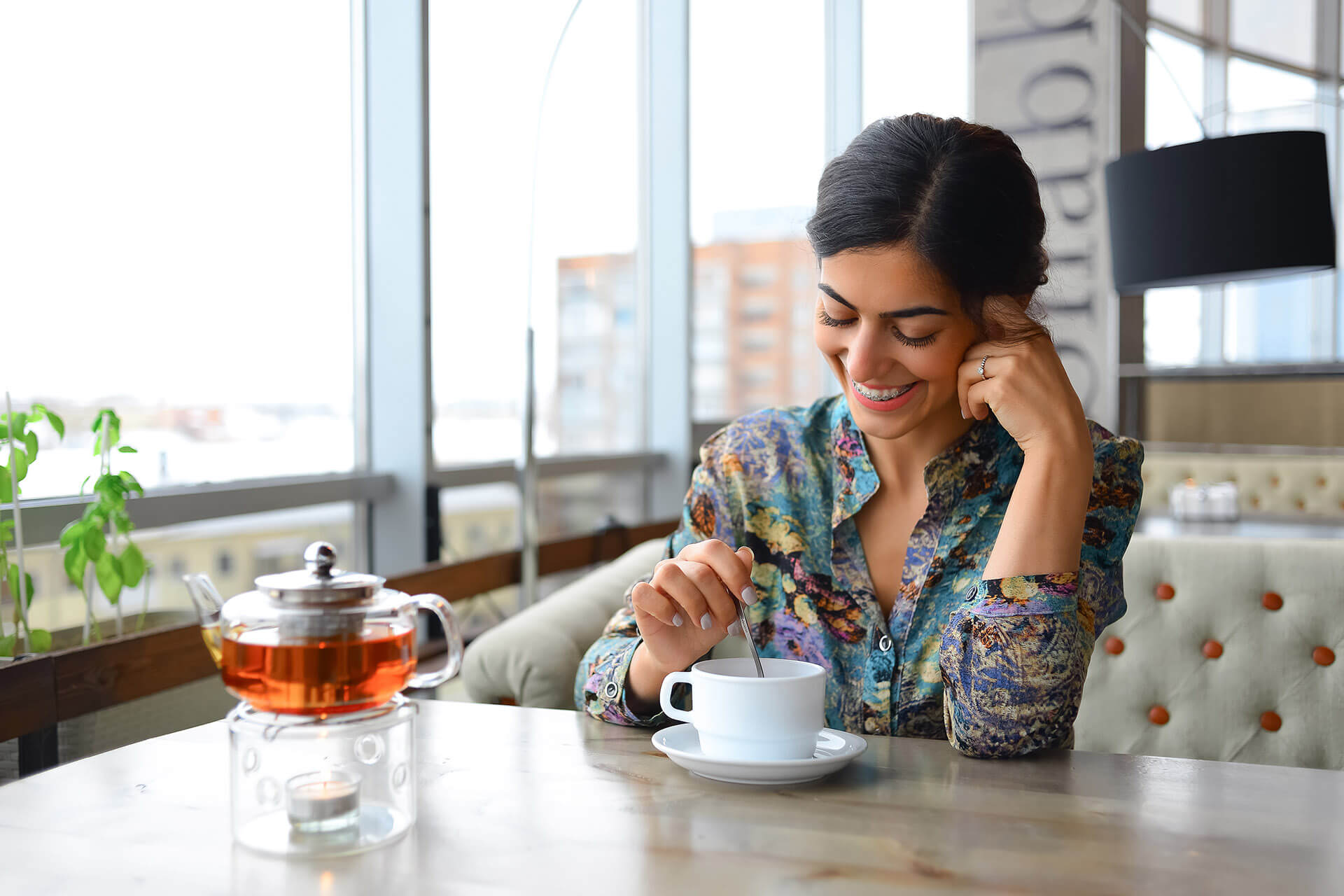 Eine Frau mit fester Zahnspange sitzt am Tisch, lacht und trinkt Tee