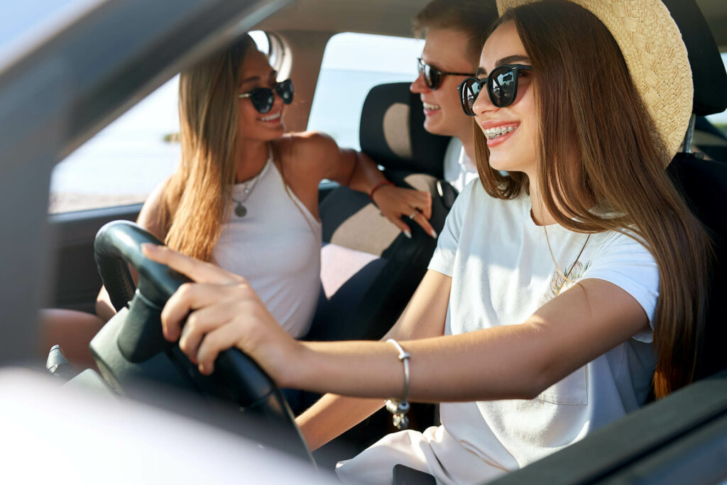 Drei junge Erwachsene mit Zahnspange sitzen im Auto und freuen sich
